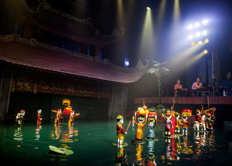 Water puppets, dressed in vibrant costumes, are controlled by puppeteers standing behind a water-filled stage.